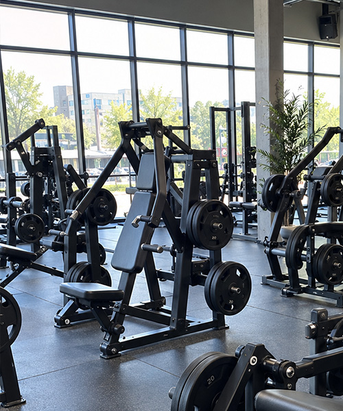 Commercial gym strength area with plate-loaded machines and stored weight plates
